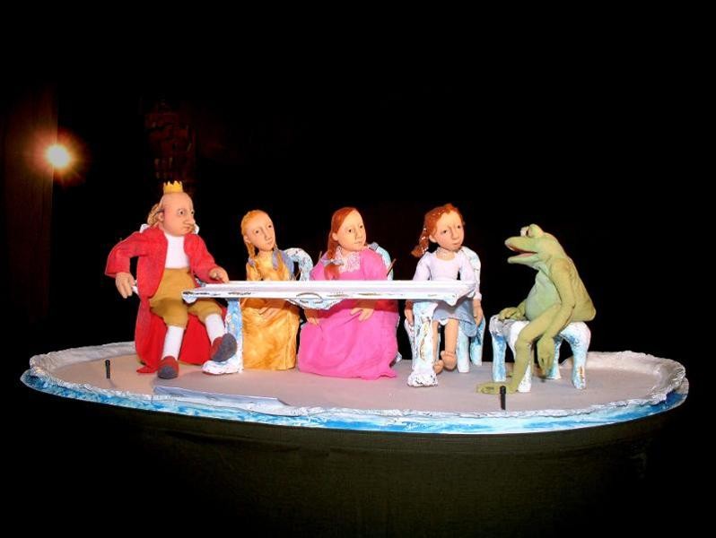 Vier Figuren sitzen mit dem Frosch an einem Tisch